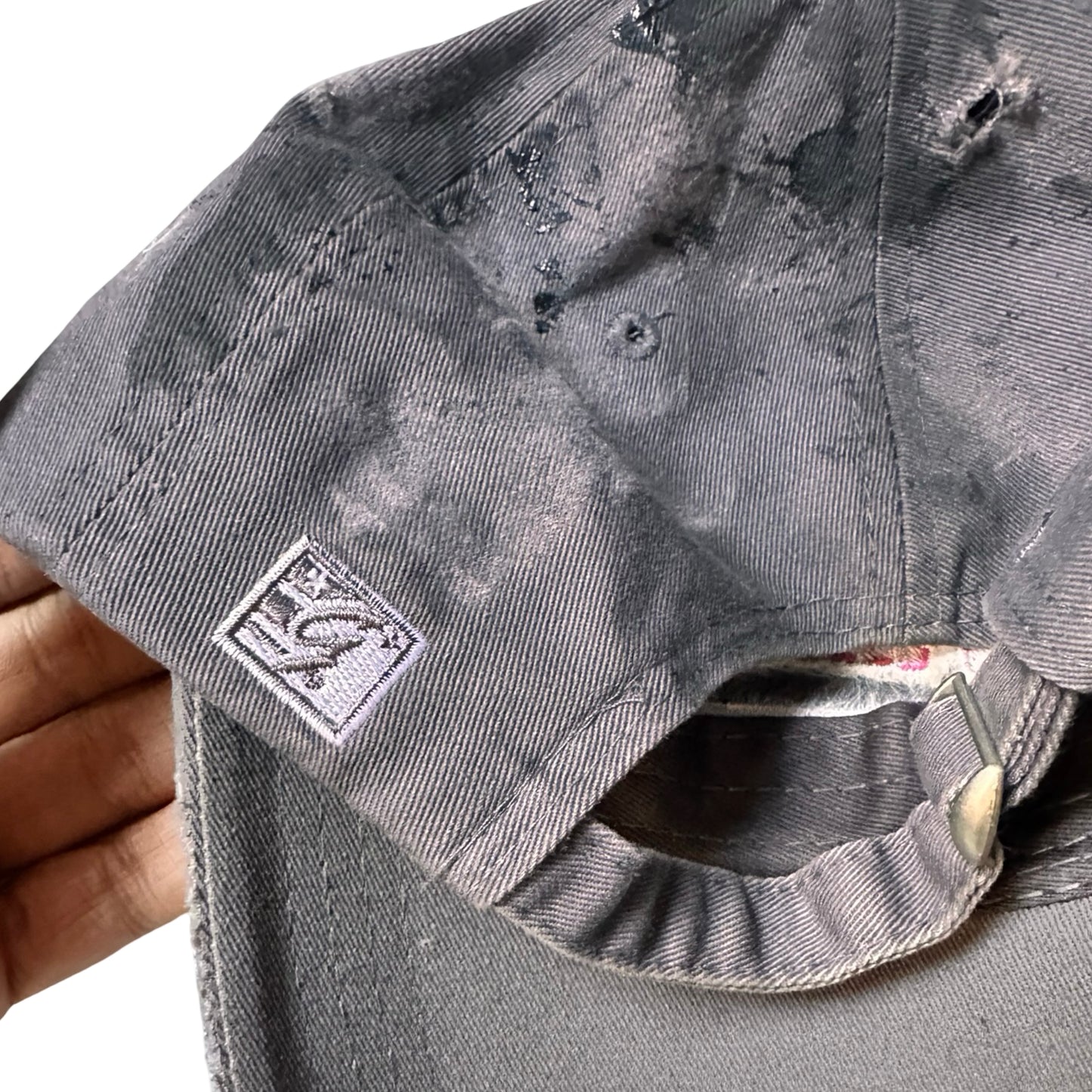 Flat back detail of Grey and pink distressed half-visor hat with ‘Los Angeles’ embroidery, black paint, and stainless steel piercings, customized by ASTROBOI*.