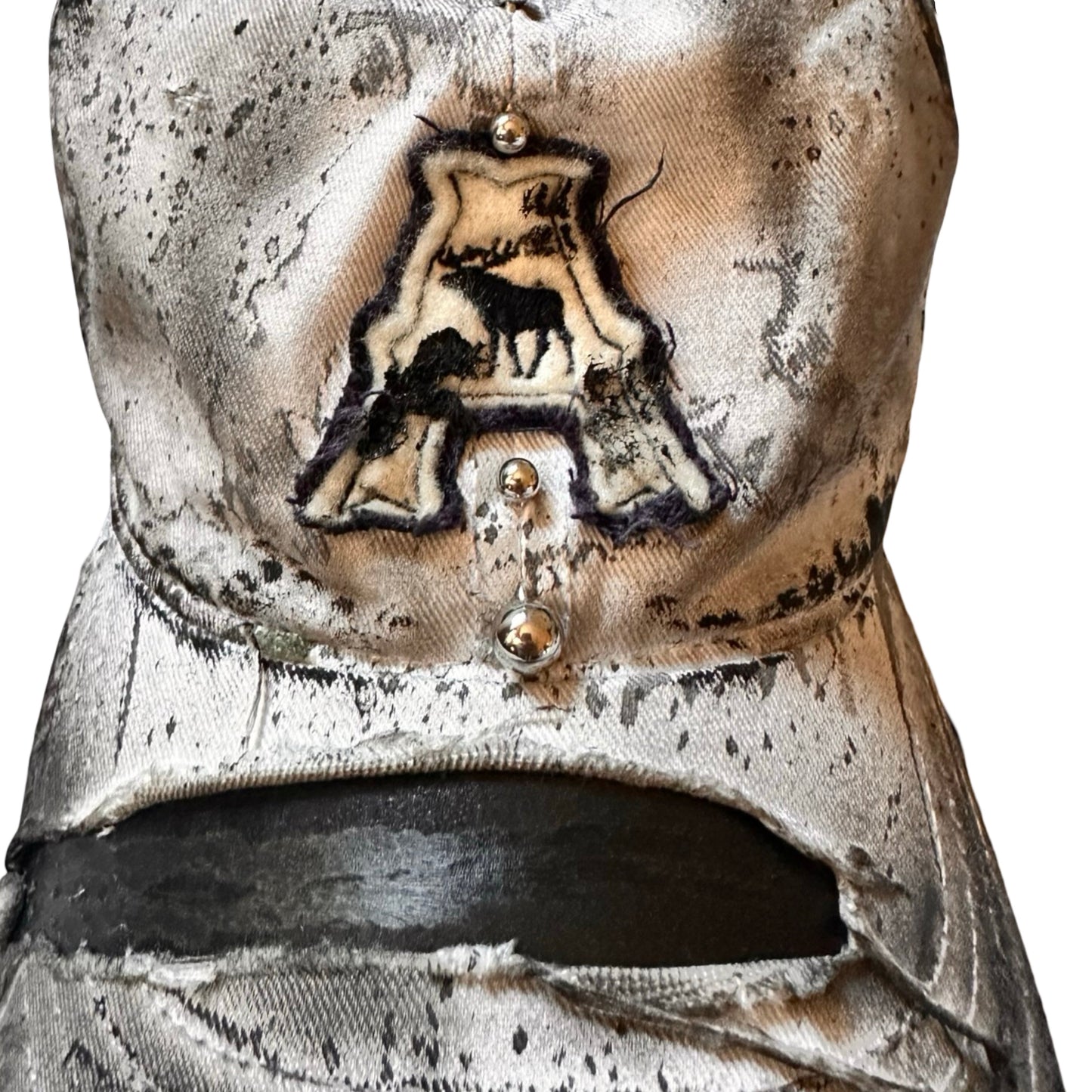 Flat close up of Off-white and black faded ASTROBOI* x Abercrombie hat with custom paint treatment and stainless steel piercing, handmade in NYC.