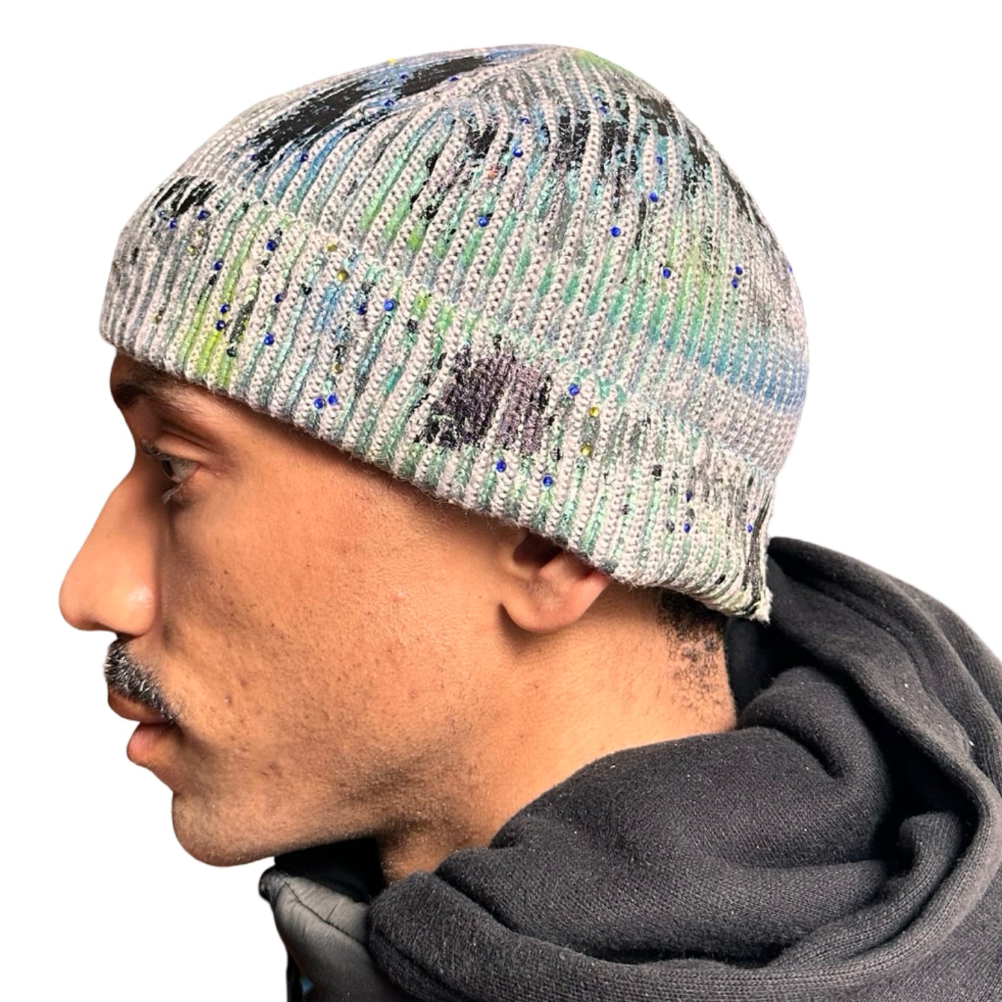 Left side of ASTROBOI* blue-green iridescent beanie featuring black metallic paint accents and tonal rhinestones, custom-made in NYC for a bold streetwear look.
