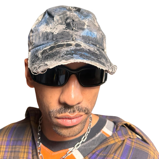 Front of Black Vuori baseball hat customized by ASTROBOI* with blue and black painted details, stainless steel piercings, and an embroidered V logo.