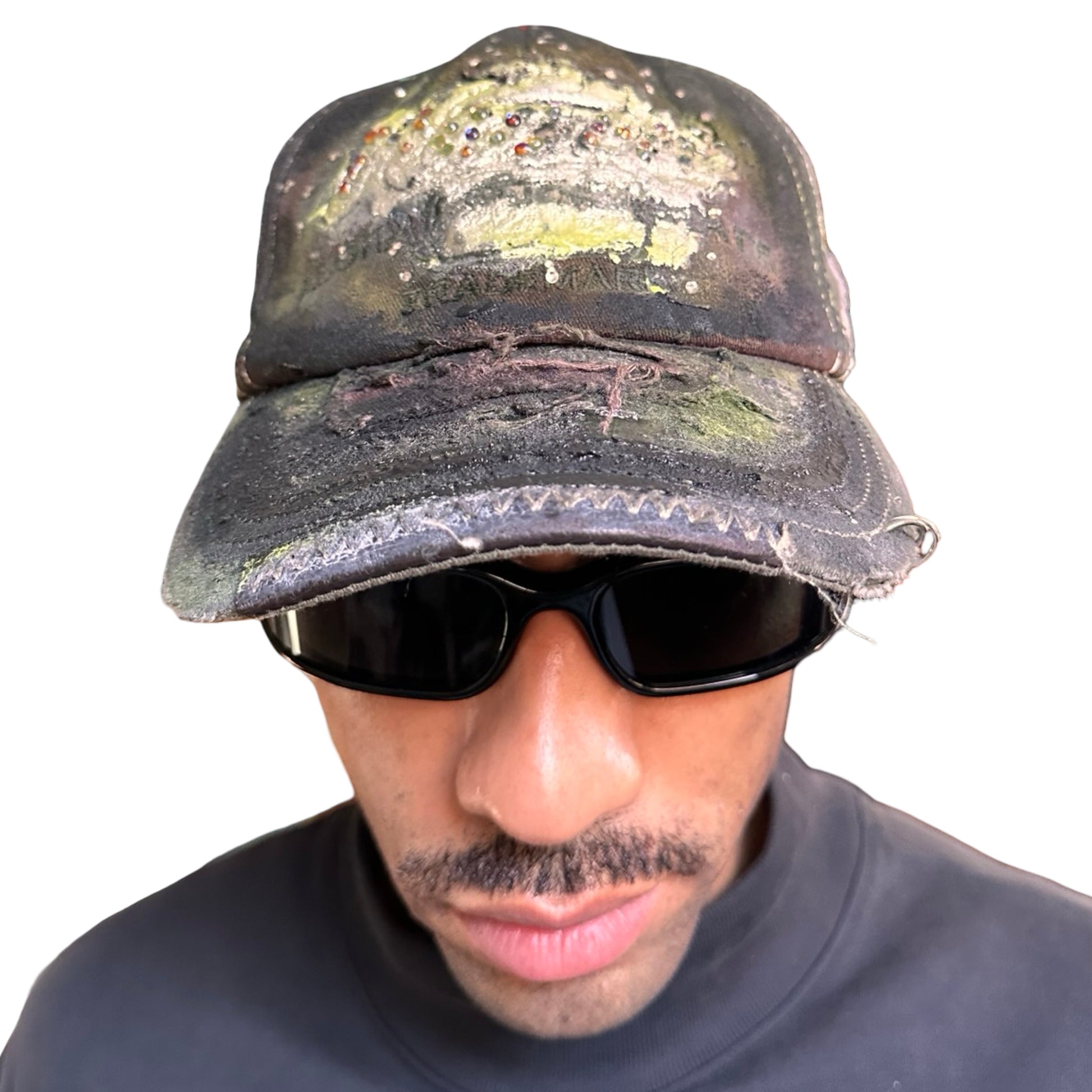 Overview of “Green and brown distressed ASTROBOI* Hawaii hat with rhinestones, metallic paint, and sterling-steel piercings, customized in NYC.”
