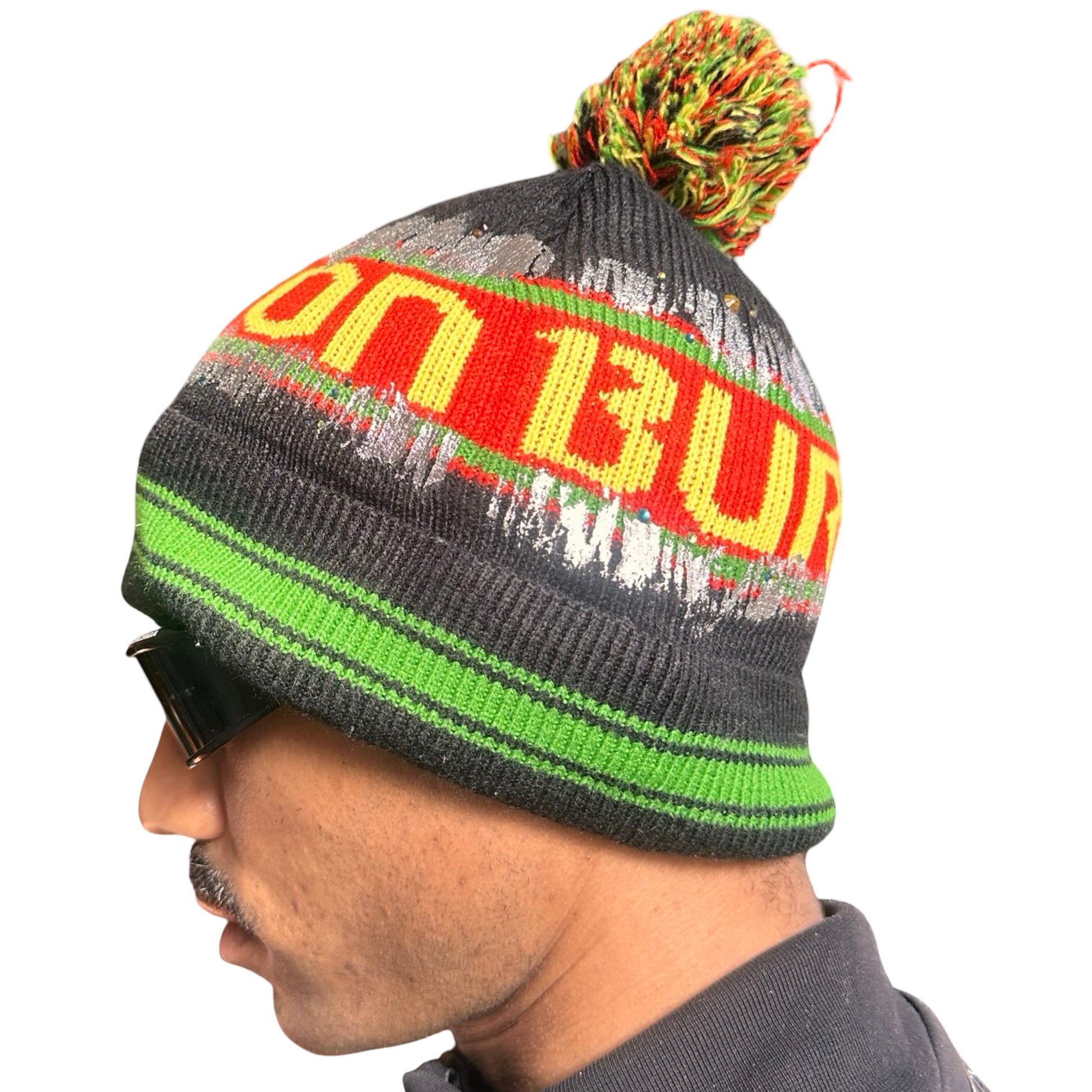 Left side of ASTROBOI* x Burton black knit Rastafarian beanie with metallic paint, rhinestones, striped pattern, and pom-pom top. Custom NYC-made winter hat.