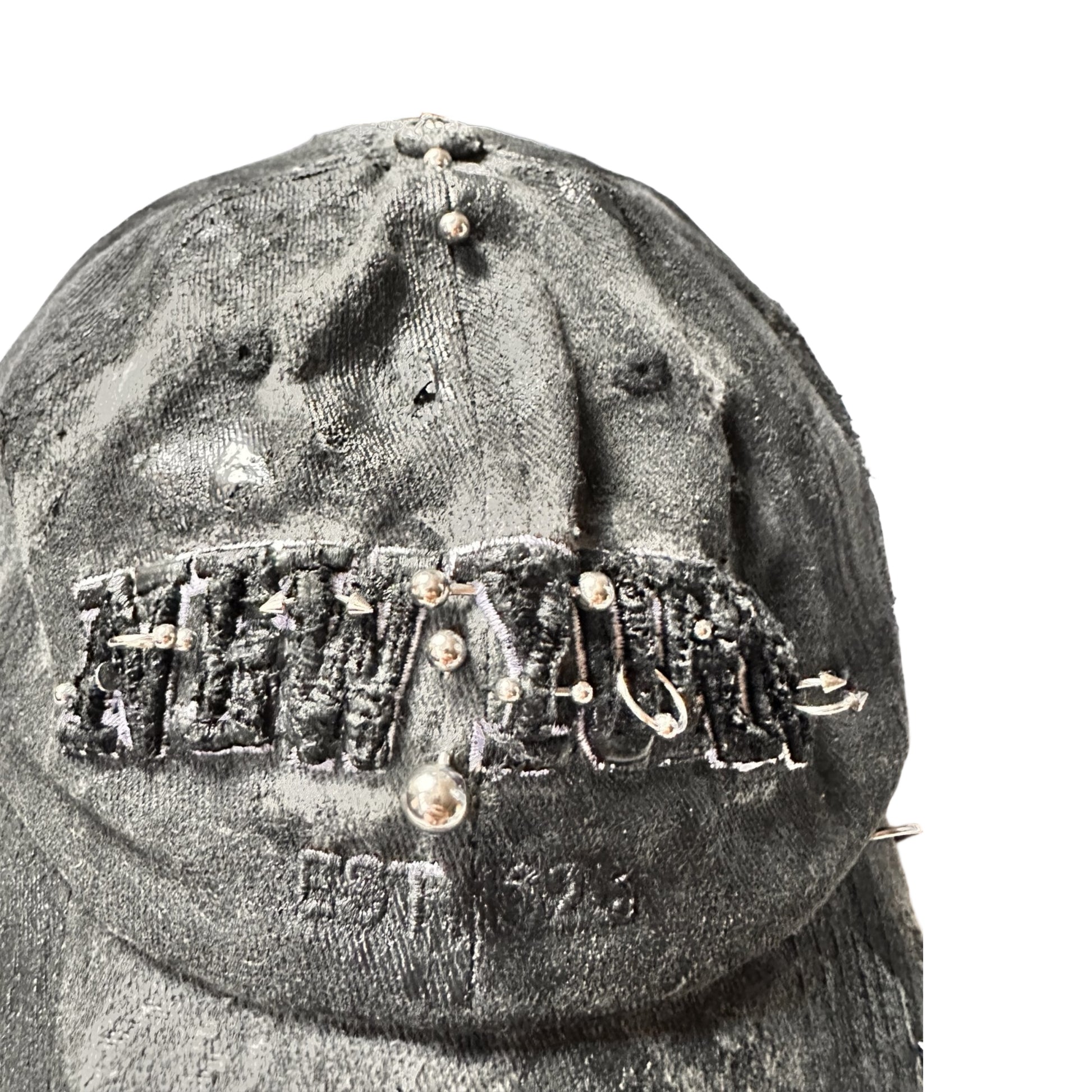 Flat front detail of Black half-visor “New York” hat with embroidered front logo, stainless steel piercings, and an adjustable strap.