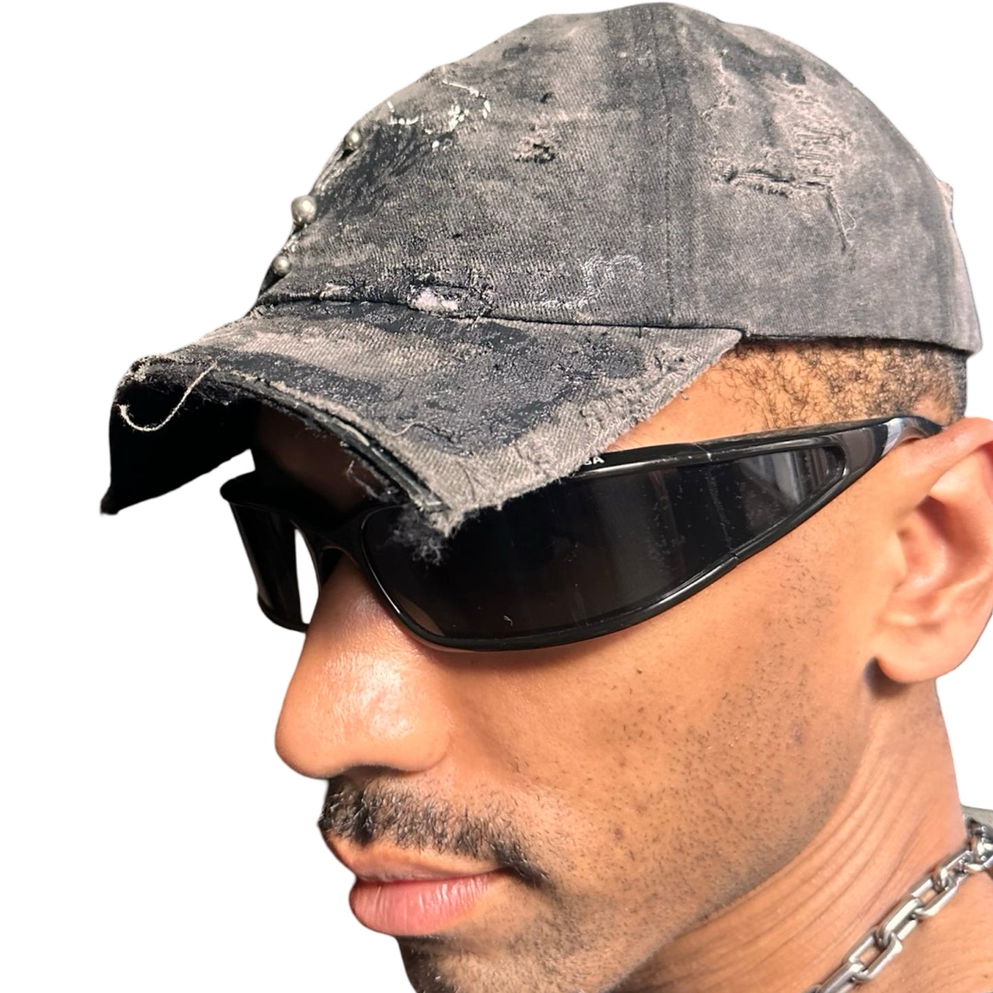 Front left side of Black distressed half-visor hat with barbed-wire logo, adjustable strap, black paint details, and stainless steel piercings along the brim.