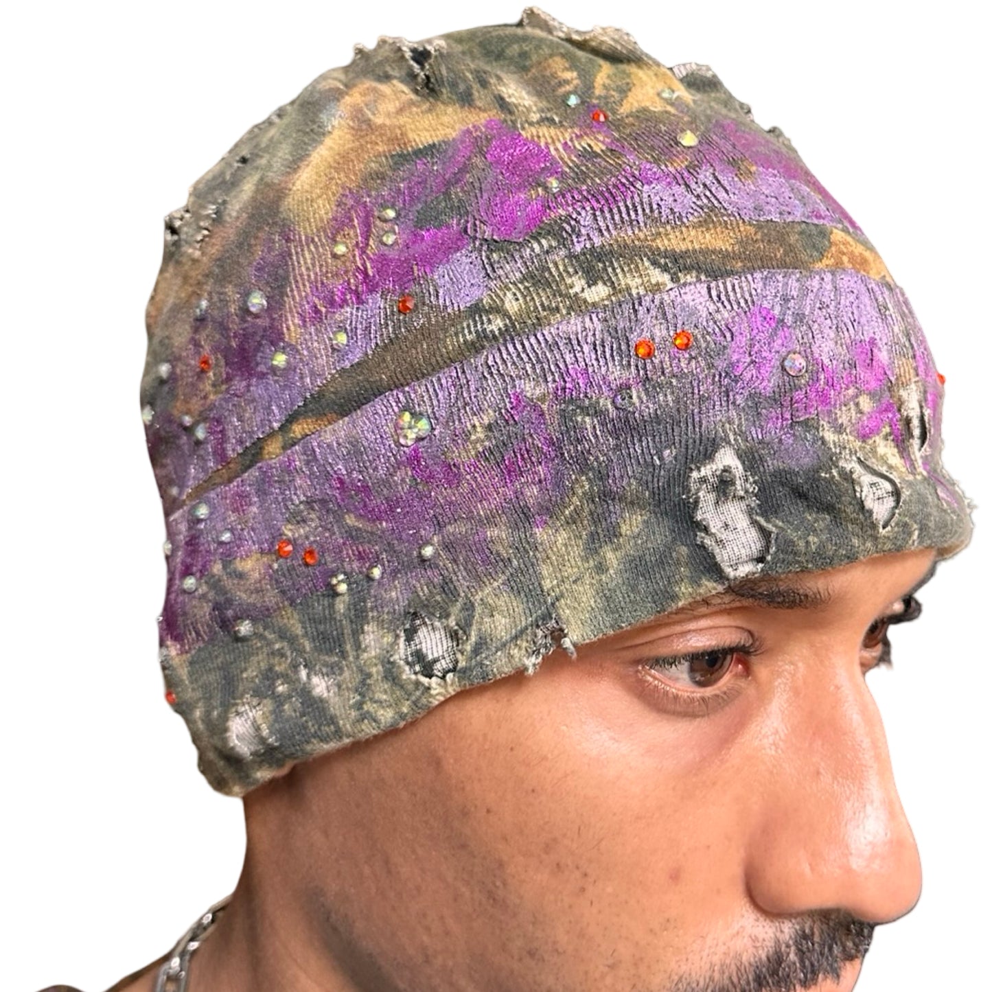 Front right side of ASTROBOI* brown RealTree grunge beanie with ripped details, lavender and magenta paint, and colorful rhinestones, handmade in NYC.