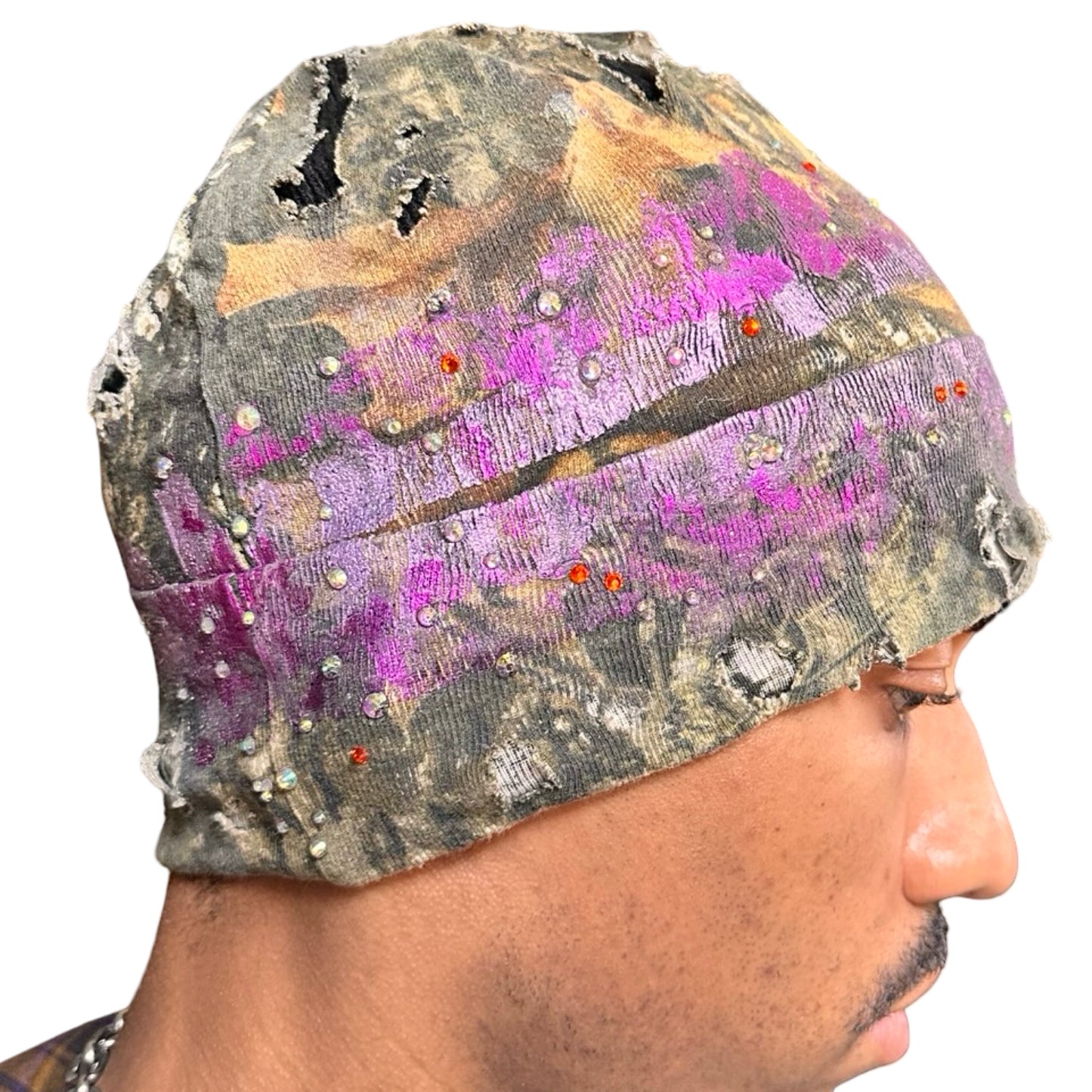 Right side of ASTROBOI* brown RealTree grunge beanie with ripped details, lavender and magenta paint, and colorful rhinestones, handmade in NYC.